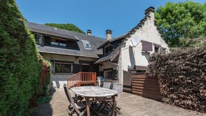 Une terrasse en bois avec une table et des chaises, un bâtiment en pierre avec un toit en pente et une clôture en bois.