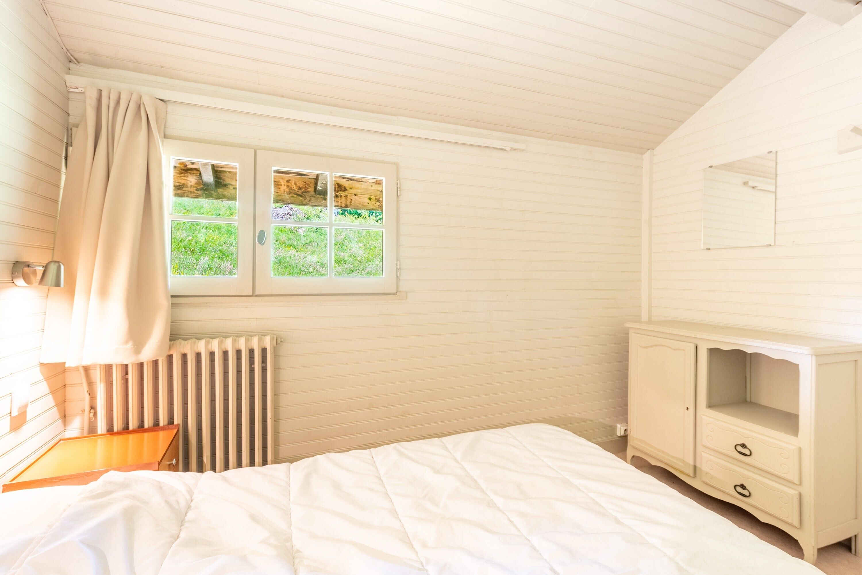 A bedroom with a bed, a window, a radiator, and a dresser.