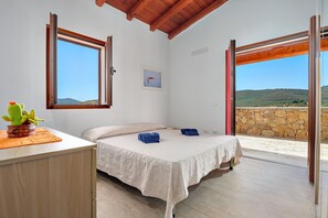 Una camera da letto con un letto, una scrivania con un cactus e vista su un muro di pietra e delle colline.