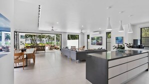 Een moderne keuken met een groot eiland, inbouwapparatuur en een eethoek met uitzicht op de tuin.