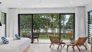 Een moderne hotelkamer met een grote schuifglazen deur die leidt naar een balkon met uitzicht op palmbomen en een wateroppervlak.