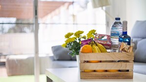 A wooden crate with fruits and a water bottle on a white table in a bright room with a view outside.