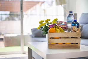 A wooden crate with fruits and a water bottle on a white table in a bright room with a view outside.