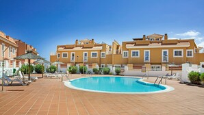 A swimming pool with lounge chairs and umbrellas, surrounded by buildings with balconies.