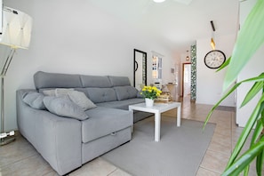 Un salon moderne avec un canapé gris, une table basse blanche et une plante en pot aux fleurs jaunes.