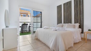 A bedroom with a bed, a small table, a chair, and a view of the outside.