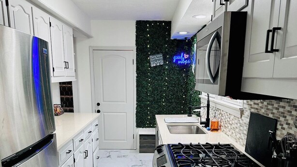 Een moderne keuken met witte kasten, een roestvrijstalen koelkast, een gasfornuis en een zwart aanrecht.