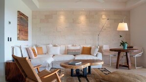 A modern living room with a white sectional sofa, a wooden coffee table, a woven armchair, and a small round table with a lamp. - Your Private Escape in Punta Mita/Premier membership, HK & Concierge Service (Hacienda de mita)