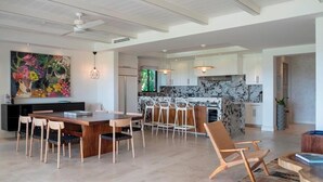 A modern kitchen with white cabinets, a marble countertop, and a dining area with a wooden table and chairs. - Your Private Escape in Punta Mita/Premier membership, HK & Concierge Service (Hacienda de mita)