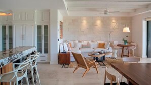 A modern kitchen with white cabinetry, a marble countertop, and a dining area with a wooden table and chairs. - Your Private Escape in Punta Mita/Premier membership, HK & Concierge Service (Hacienda de mita)