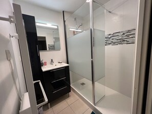 Ein modernes Badezimmer mit Duschkabine aus Glas, einem weißen Waschbecken und einem schwarzen Waschtisch.