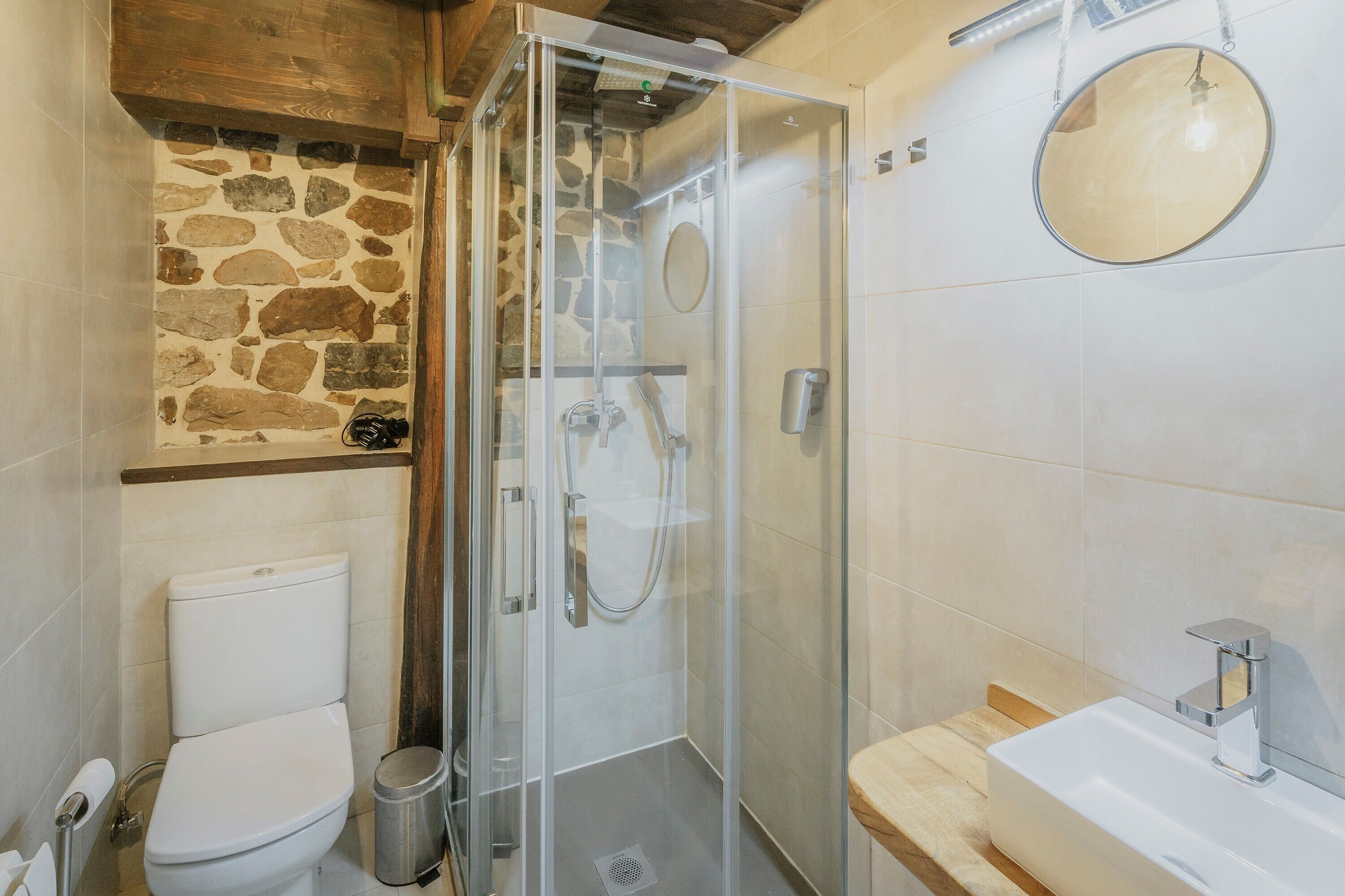 Ein Badezimmer mit Duschkabine, Toilette, Waschbecken und Steinwand.