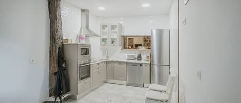 A modern kitchen with white cabinets, a built-in oven, microwave, and refrigerator.