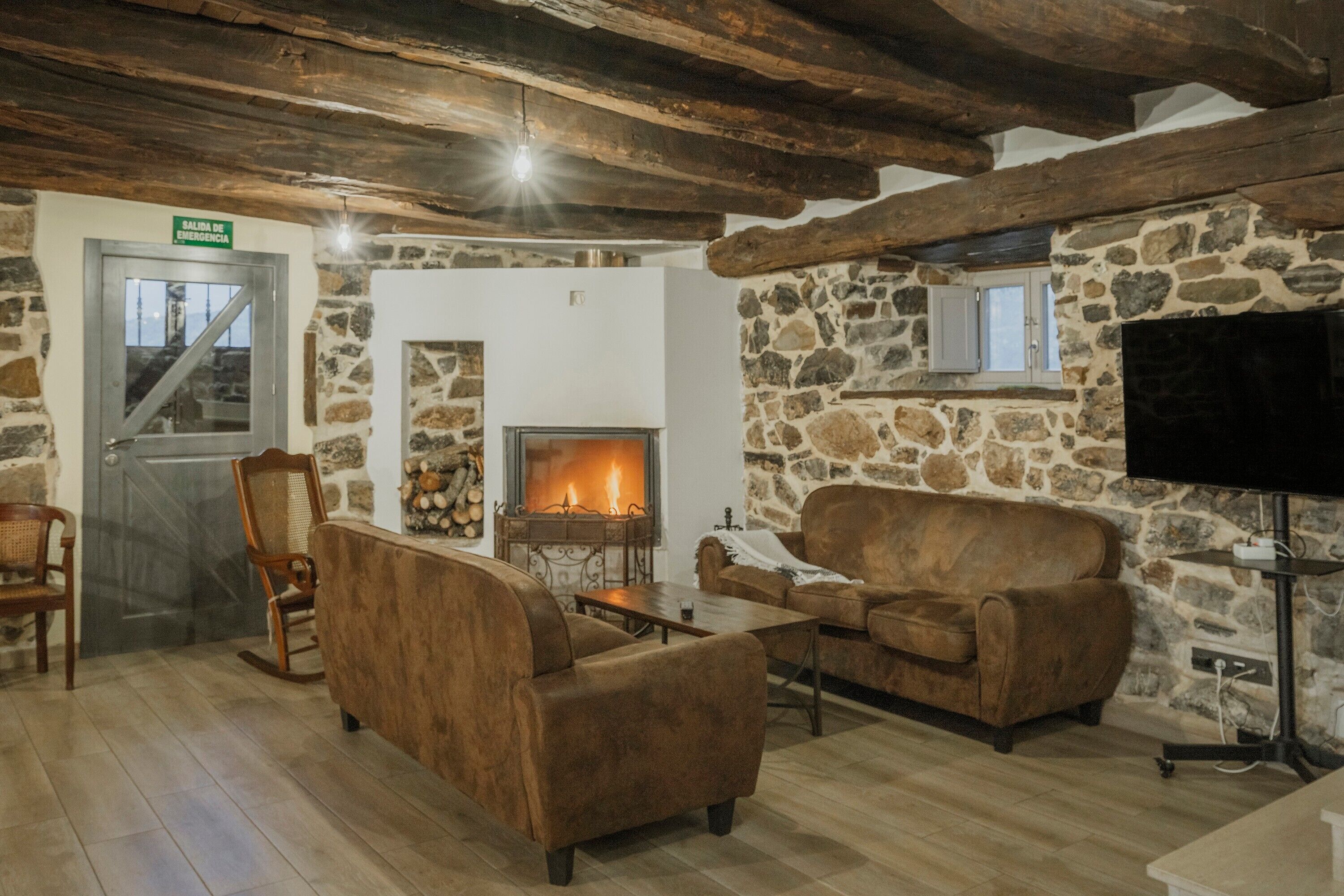 A cozy room with a fireplace, stone walls, wooden beams, a television, and a sofa.