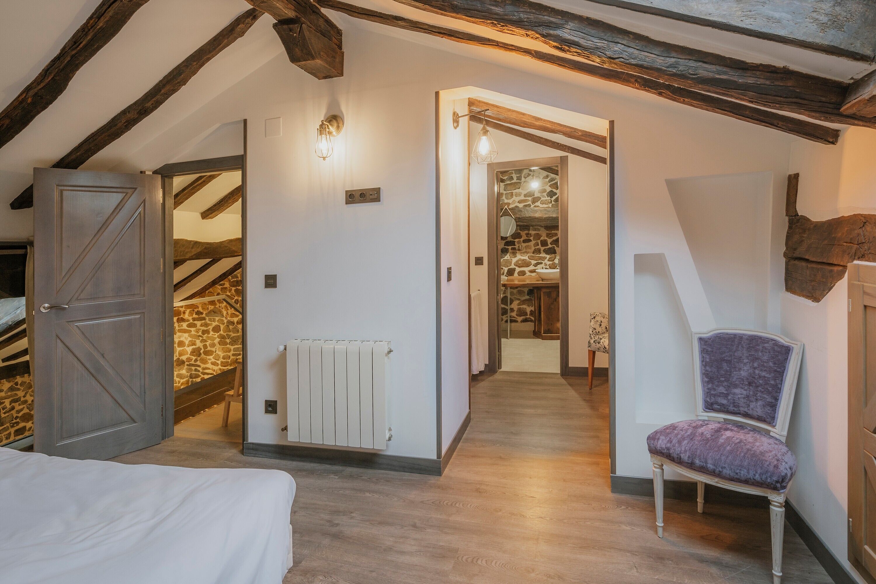 Een slaapkamer met een bed, een stoel, een radiator en een stenen muur.