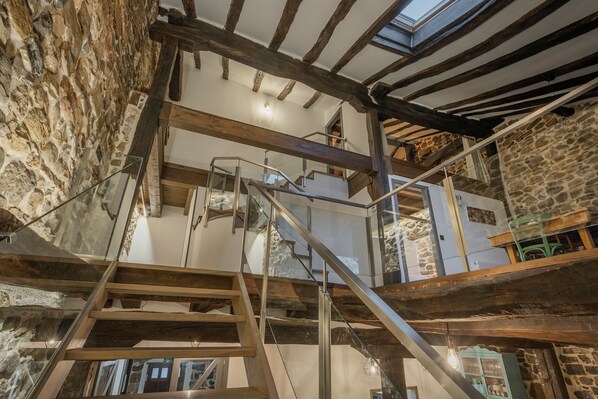 A rustic interior with exposed stone walls, wooden beams, and a staircase with glass railings.