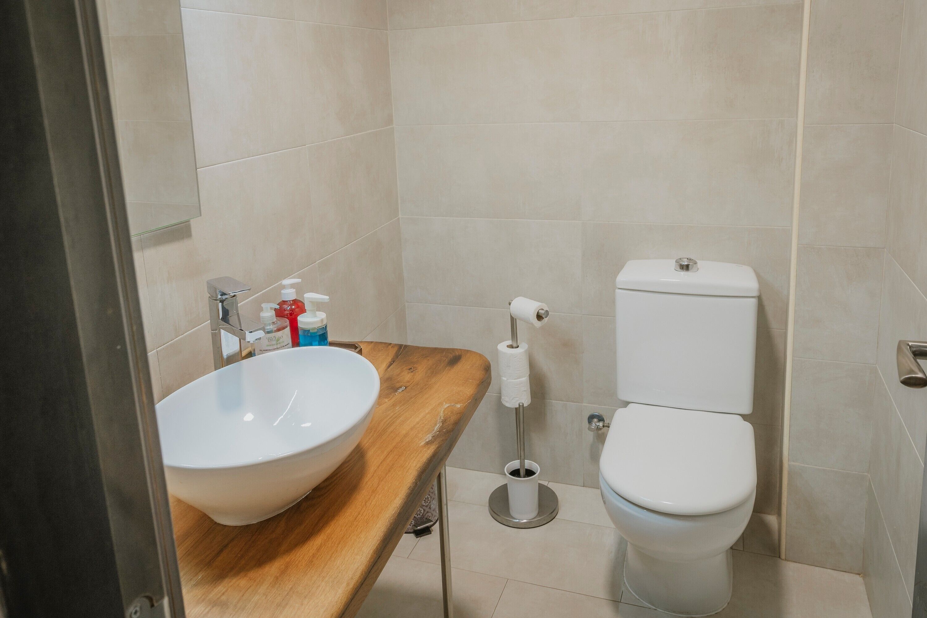 Une salle de bain avec un meuble-lavabo en bois, un lavabo blanc, des toilettes et un sèche-mains.