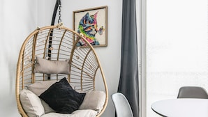A room with a wicker hanging chair, a white table, a gray chair, and a colorful painting on the wall. - Holiday Home 'Bright' with Mountain View, Balcony and Wi-Fi (Agaete)