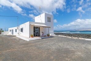 Un bâtiment blanc dot é d’un petit porche, d’une porte et d’une fenêtre, situé près d’une côte rocheuse.