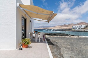 A white building with a patio, a table, chairs, a potted plant, and a beach view. - Holiday Home 'La Casita Del Mar' Seafront, Private Terrace & Wi-Fi (Caleta de Caballo)