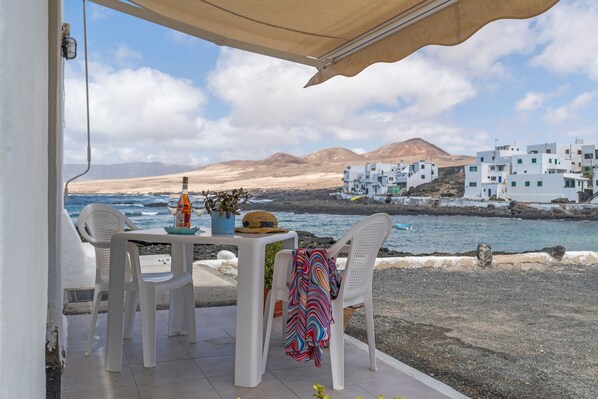Une terrasse extérieure avec une table, des chaises et une vue sur la mer et les bâtiments blancs.