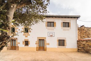 Ein Gebäude mit weißer Fassade, mehreren Fenstern, einer Tür und einem Basketballkorb.