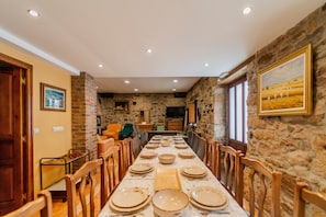 A long dining table set for a meal in a room with stone walls, wooden furniture, and recessed ceiling lights.