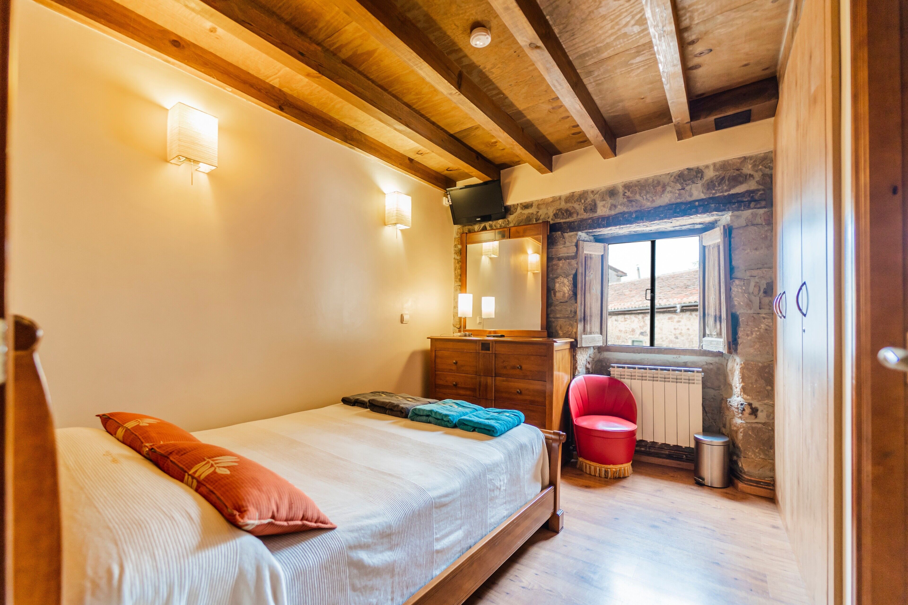 Une chambre à coucher avec un lit en bois, une commode, une chaise rouge, un miroir et une fenêtre donnant sur un beau paysage.