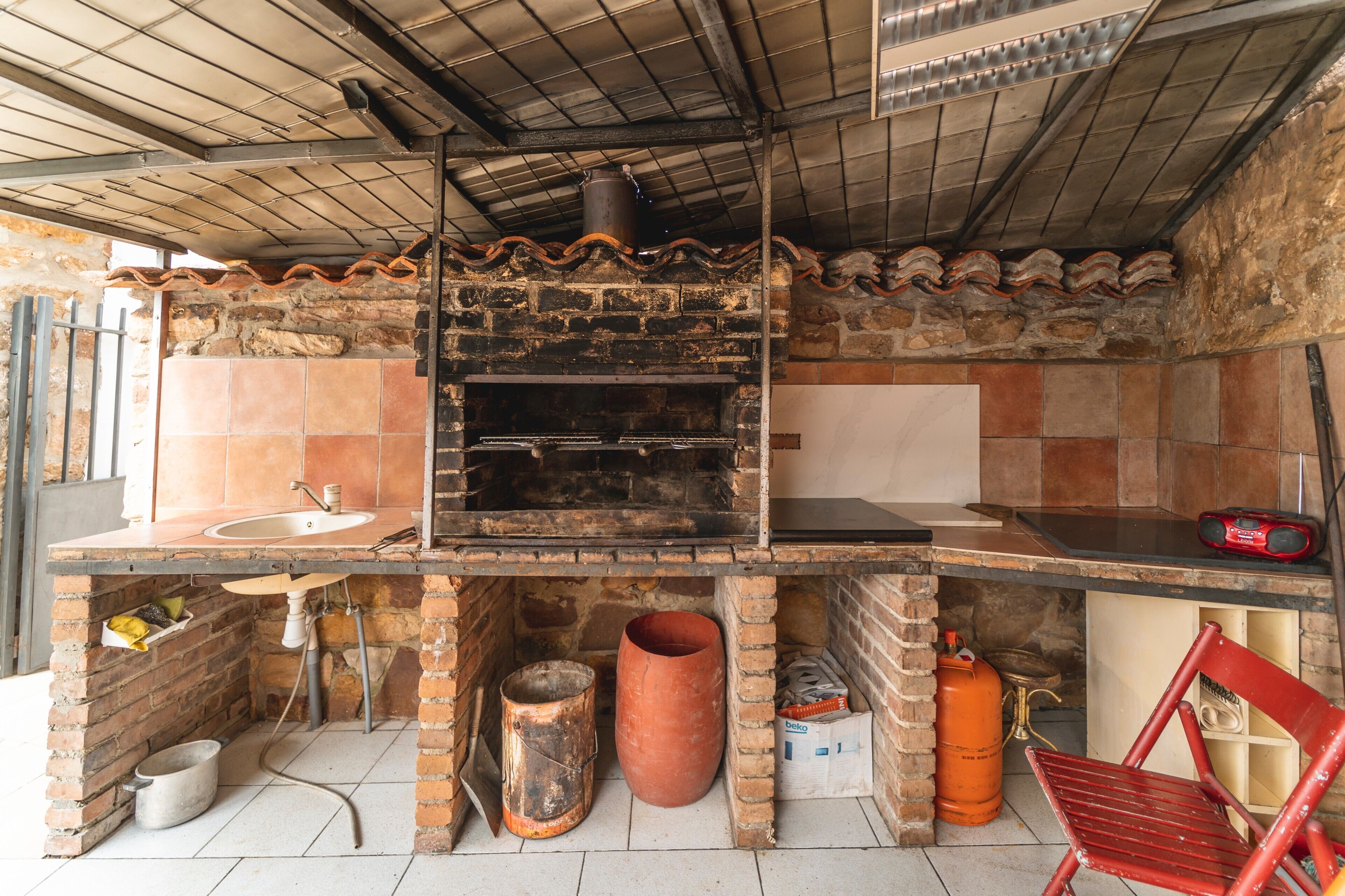 A kitchen with a brick oven, a sink, and a red chair.