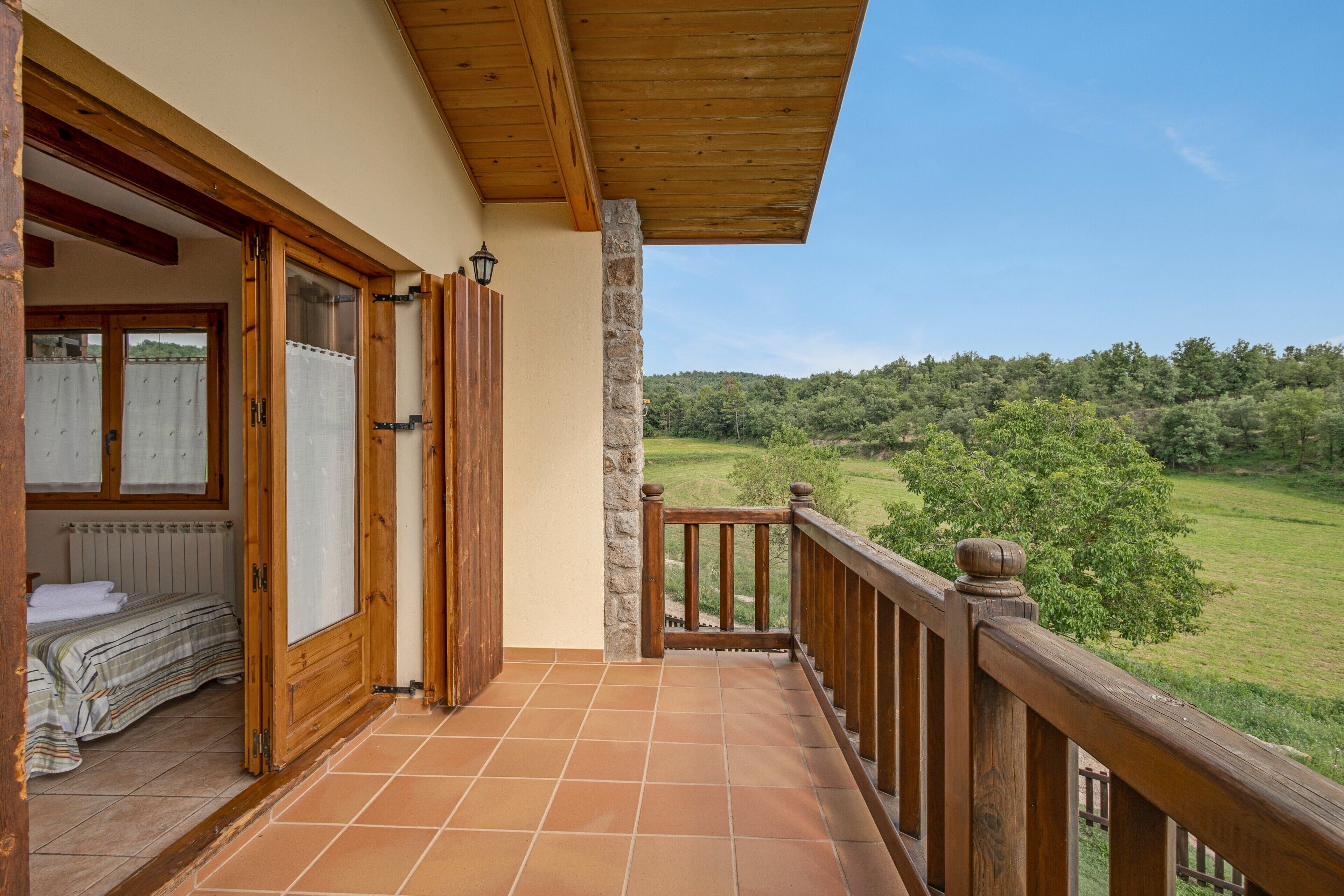 Un balcon avec une balustrade en bois, un lit recouvert d’une couvre-lit à rayures et une vue sur un paysage verdoyant.