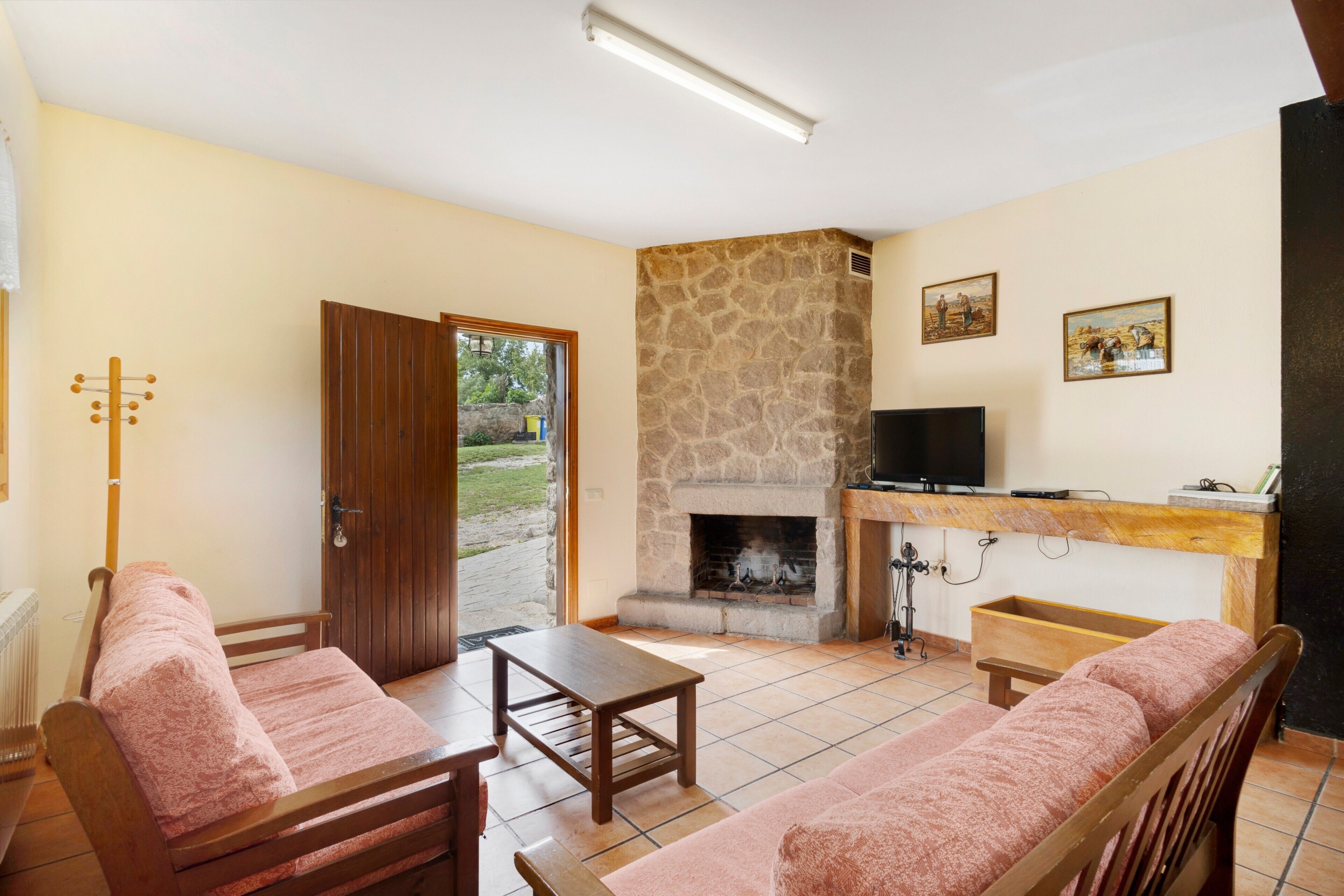 Una habitación con chimenea de piedra, muebles de madera, televisor y puerta que da al exterior.