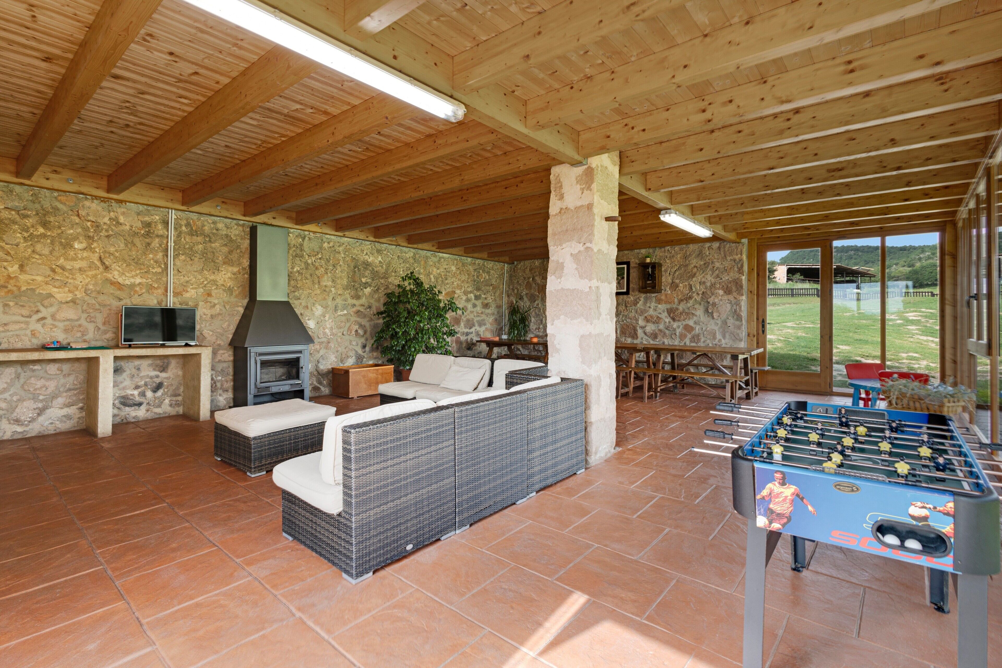 Un área recreativa interior con una mesa de fútbol de mesa, un sofá, una chimenea y paredes de piedra.