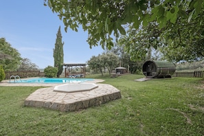 A backyard with a swimming pool, stone patio, and a barrel.