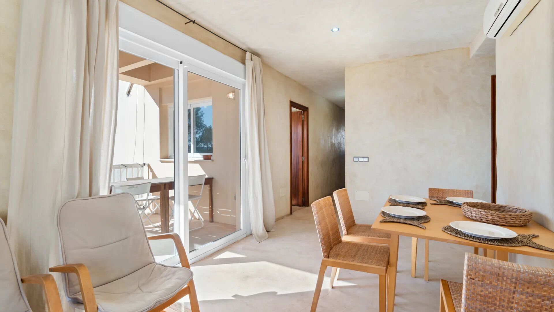Un comedor con una mesa dispuesta para cuatro, sillas y vistas al exterior a través de un ventanal.