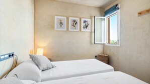 Une chambre avec deux lits, une lampe de chevet, une fenêtre donnant sur un beau paysage et trois illustrations botaniques encadrées accrochées au mur.