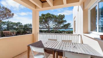 Un balcón con mesa y sillas de madera, con vistas a un paisaje pintoresco de árboles y el mar.