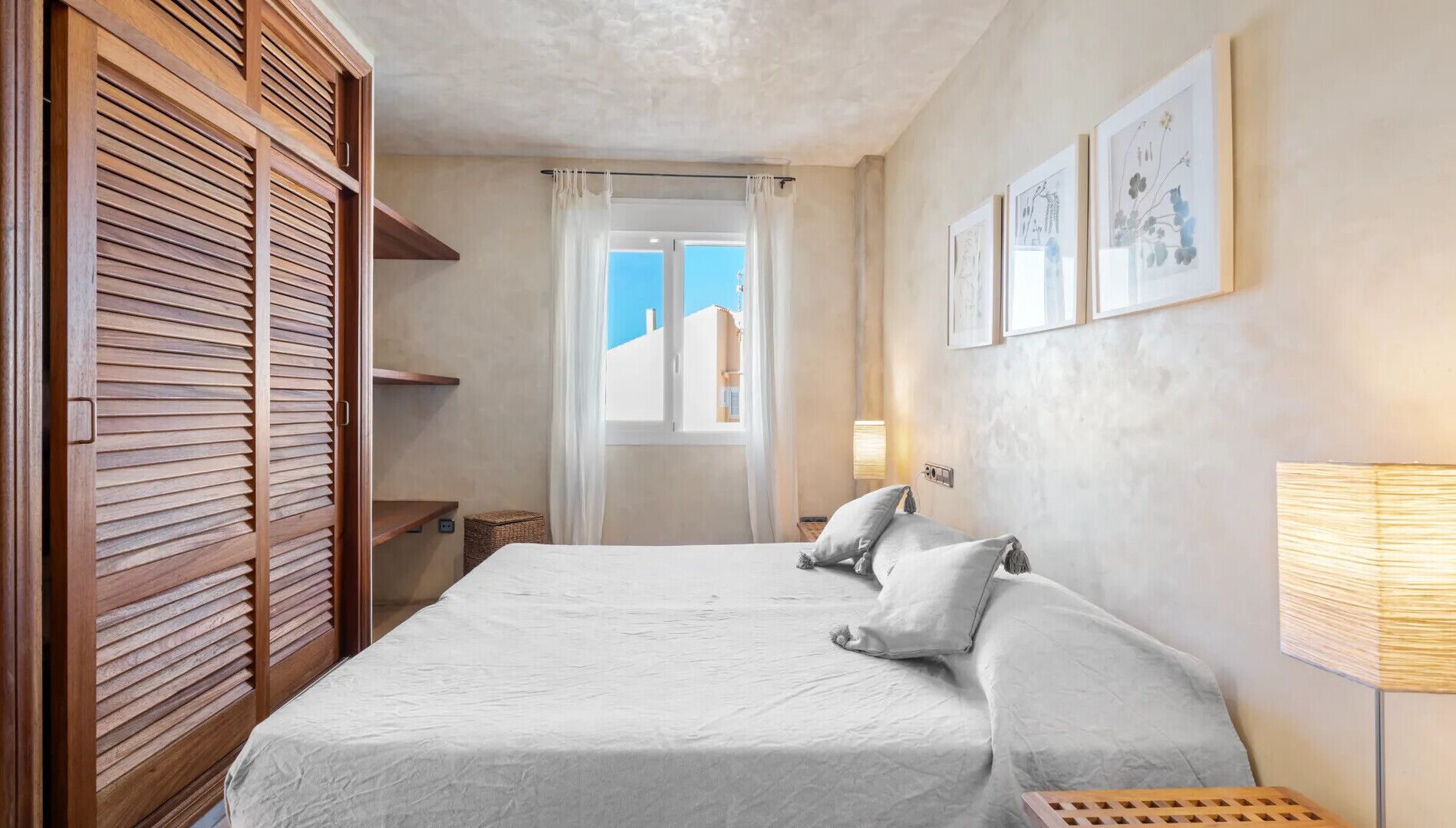 Un dormitorio con cama, armario de madera, ventana con vistas y una obra de arte en la pared.