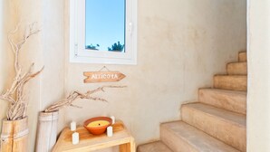 A staircase with a wooden sign reading "ATTICO 1A" above it, a small table with candles and a bowl, and a window with a view of blue sky and plants. - Vista Azul Duplex 1 Formentera (La Savina)