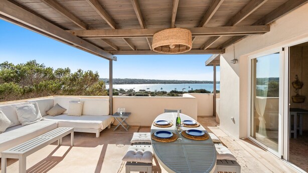 A covered outdoor seating area with a table set for two, overlooking a body of water. - Vista Azul Duplex 1 Formentera (La Savina)