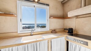 A compact kitchen with a window overlooking a scenic view, a sink, a Bosch stove, and a coffee maker. - Vista Azul Duplex 1 Formentera (La Savina)