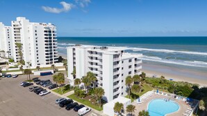 A beachfront hotel with multiple high-rise buildings, a parking lot, and a swimming pool. - Updated direct oceanfront corner 2/2 with a large balcony and heated beachfront pool (New Smyrna Beach)