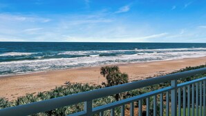 A beach with waves, a clear sky, and a white railing. - Updated direct oceanfront corner 2/2 with a large balcony and heated beachfront pool (New Smyrna Beach)