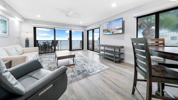 A spacious living area with a balcony, a dining table, and a sofa. - Updated direct oceanfront corner 2/2 with a large balcony and heated beachfront pool (New Smyrna Beach)