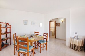 A dining area with a round table, wooden chairs, a bookshelf, and a small table with a lamp.