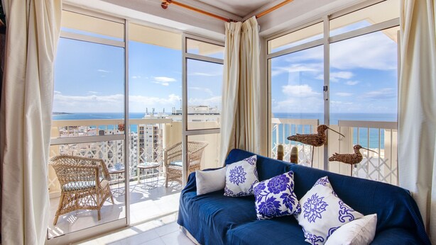 Un balcon avec un canapé, des fauteuils en osier et une vue sur la mer.
