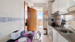 Une cuisine avec des meubles blancs, un grille-pain, un évier et une vue sur l’extérieur, visible à travers une porte ouverte.