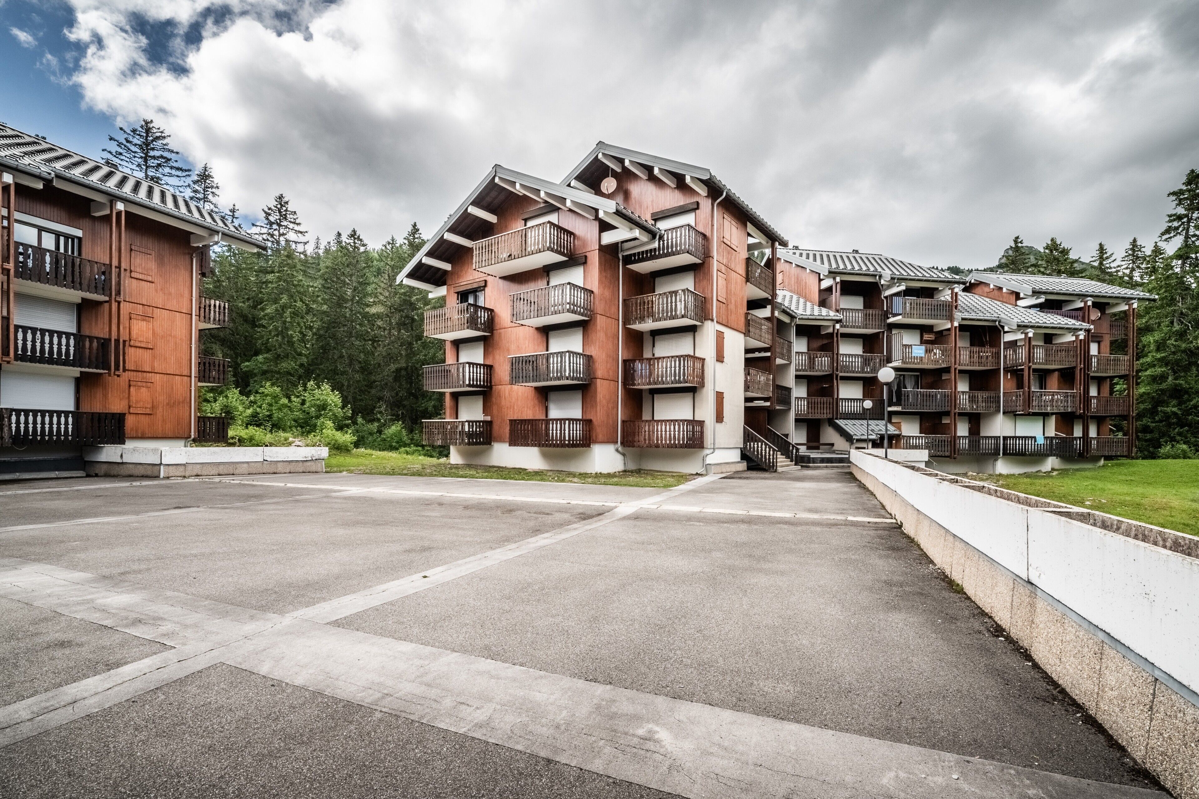 A multi-story hotel with balconies, a parking area, and a view of trees.