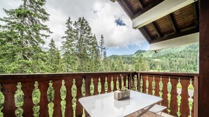 A balcony with a table and chairs, a wooden railing, and a view of a forested mountain. - Apartment 'Fleury' with Mountain View and Balcony (Mieussy)