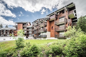 A multi-story building with balconies, a grassy courtyard, and surrounding greenery.