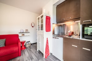 A compact kitchen with modern appliances, a red sofa, and a small dining area. - Apartment 'Fleury' with Mountain View and Balcony (Mieussy)